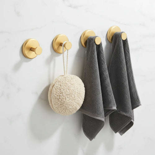 Four brushed gold suction hooks on a white marble wall holding a sponge and two grey hand towels
